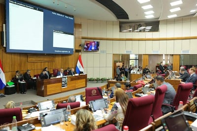 Grupo de seis hombres discutiendo en el Senado, con banderas de Paraguay visibles, rodeados de documentos y dispositivos electrónicos.