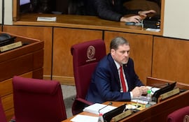 Natalicio Esteban Chase Acosta sentado en sesión, vestido con traje oscuro y corbata roja, rodeado de documentos y micrófono.