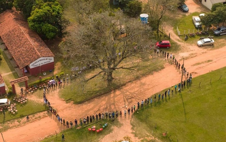 Treinta personas rodean un gran árbol, escuchando atentamente a un orador en un ambiente rural junto a la Escuela Básica N° 1407.