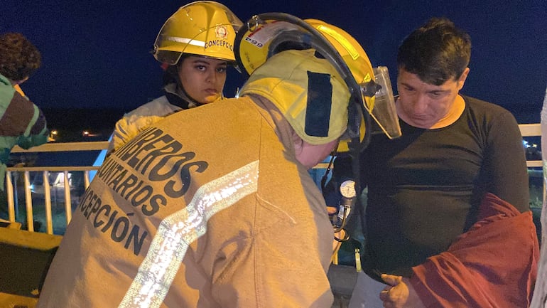 Bomberos con cascos amarillos atienden a un hombre preocupado con prenda roja en ambiente urbano nocturno.