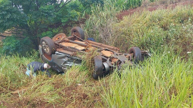 Hombre en chaqueta oscura agachado junto a la ambulancia volcada, en medio de una zanja.