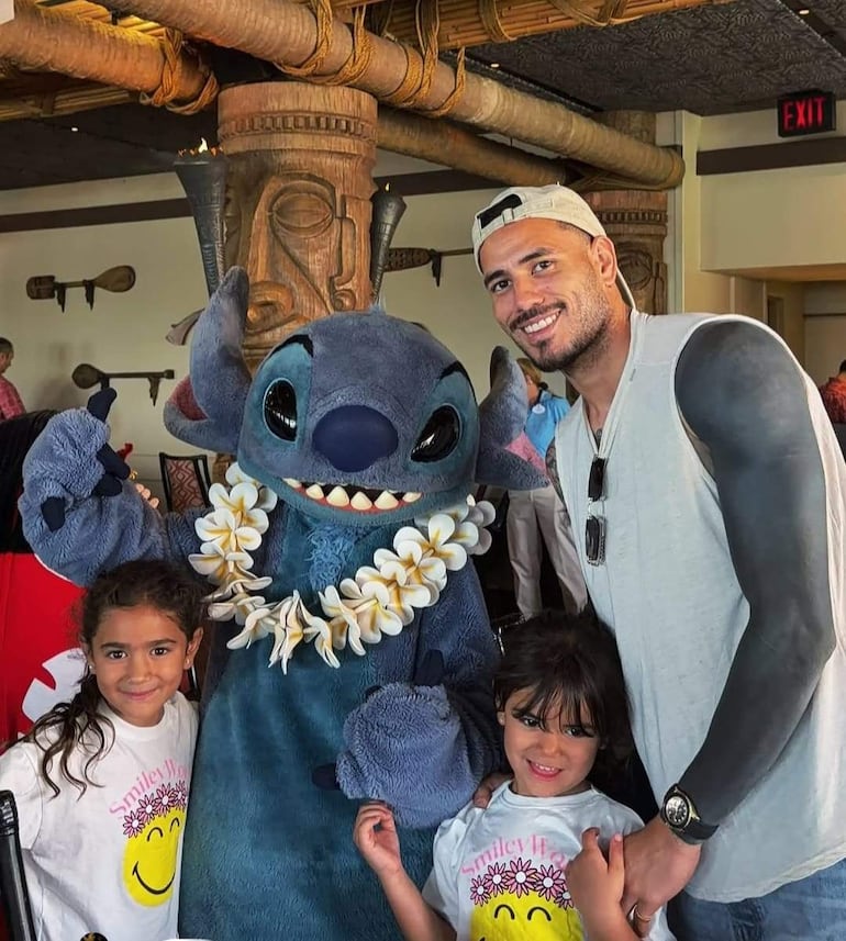 Antonio Sanabria sonríe con dos niñas en camisetas blancas mientras posan junto a un personaje disfrazado de 'Stitch'.