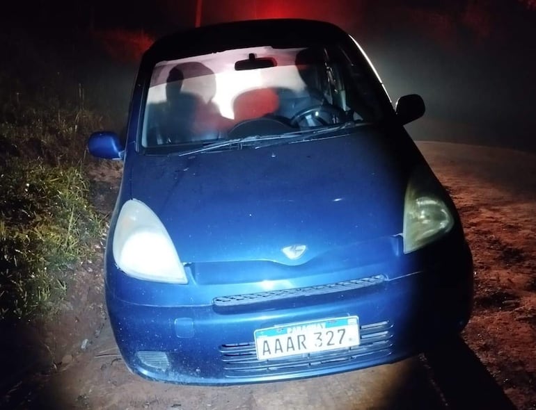 Vehículo azul estacionado en área rural, con matrícula 'AAAR 327', luces de fondo envuelven el ambiente en neblina.