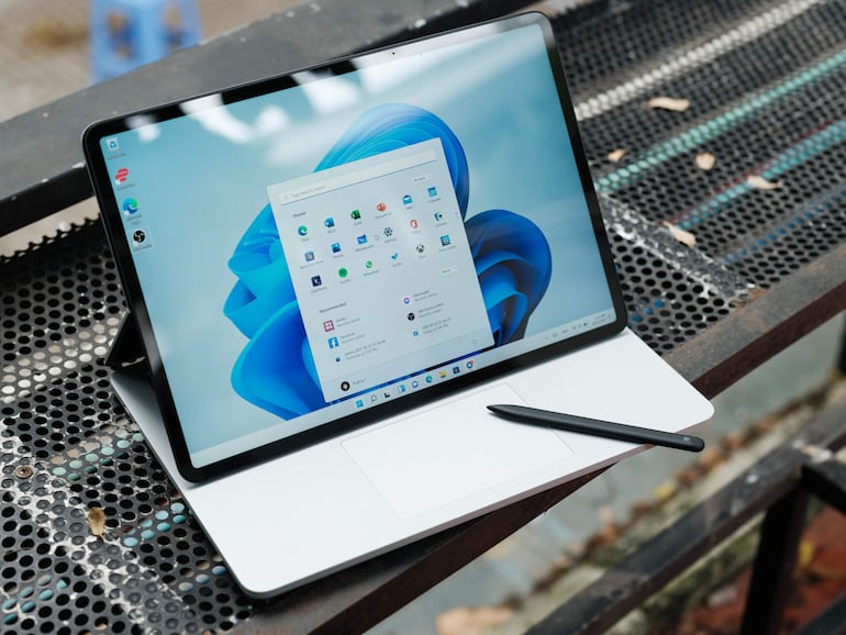 Dispositivo electrónico con pantalla de Windows 11 sobre una superficie metálica, complementado con un lápiz óptico negro.