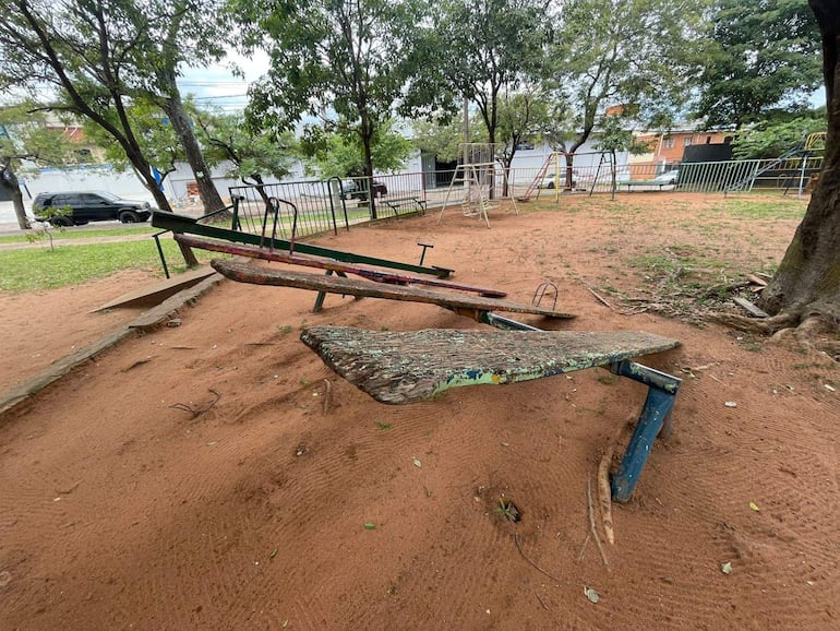 Playground de Plaza Lola de Miño con balancines de colores desgastados y vegetación circundante, sin personas presentes.