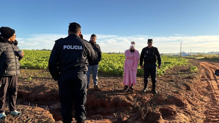Dos agentes de policía conversan con un menor con manta rosa en un campo despejado, mientras un hombre observa la escena.