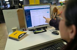 Persona con cabello oscuro y gafas, señalando pantalla de computadora en oficina, rodeada de útiles y cuaderno con 'abc 2025'.