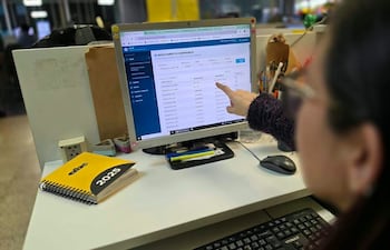 Persona con cabello oscuro y gafas, señalando pantalla de computadora en oficina, rodeada de útiles y cuaderno con 'abc 2025'.