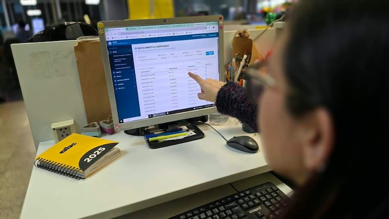 Persona con cabello oscuro y gafas, señalando pantalla de computadora en oficina, rodeada de útiles y cuaderno con 'abc 2025'.