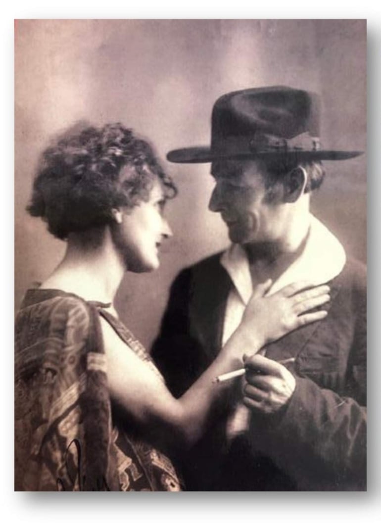 Josefina de cabello rizado y blusa decorativa toca el pecho de Julián, que viste una camisa blanca y abrigo oscuro, compartiendo un momento íntimo.