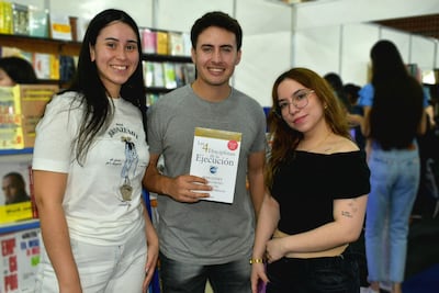 Mujeres sonrientes acompañan a un hombre que sostiene 'Las 4 Disciplinas de la Ejecución' en un entorno de feria del libro.