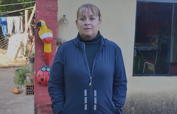 Mujer en chaqueta azul oscura, con expresión seria, espera en un entorno ajardinado con decoraciones de plástico.