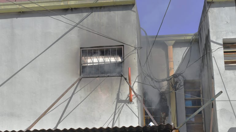 Humo sale de una ventana del depósito 'El Petiso' en un entorno urbano con cables eléctricos visibles.