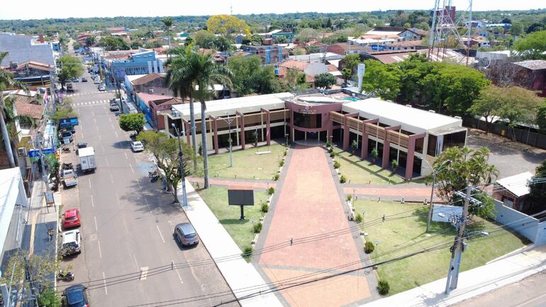Edificio moderno de la municipalidad de Coronel Oviedo, rodeado de vegetación y banderas en su fachada.