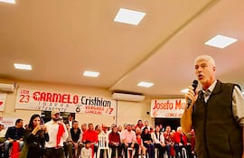 Arnoldo Wiens en el podio con micrófono, rodeado de una audiencia vestida de rojo, algunas personas grabando el evento.