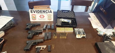 Mesa con cuatro pistolas y municiones, señal de 'EVIDENCIA' del Ministerio Público en un ambiente de investigación.