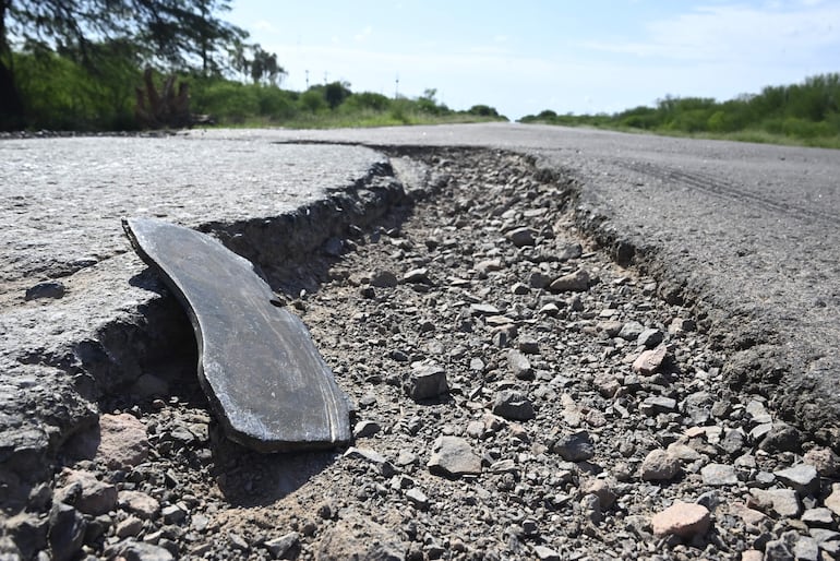 Tramo de carretera deteriorada con hendiduras visibles y acumulación de grava en ambiente rural.
