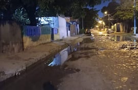 Calle empedrada con charcos reflejando luz de farolas, y un automóvil estacionado al fondo. No hay personas en la escena.