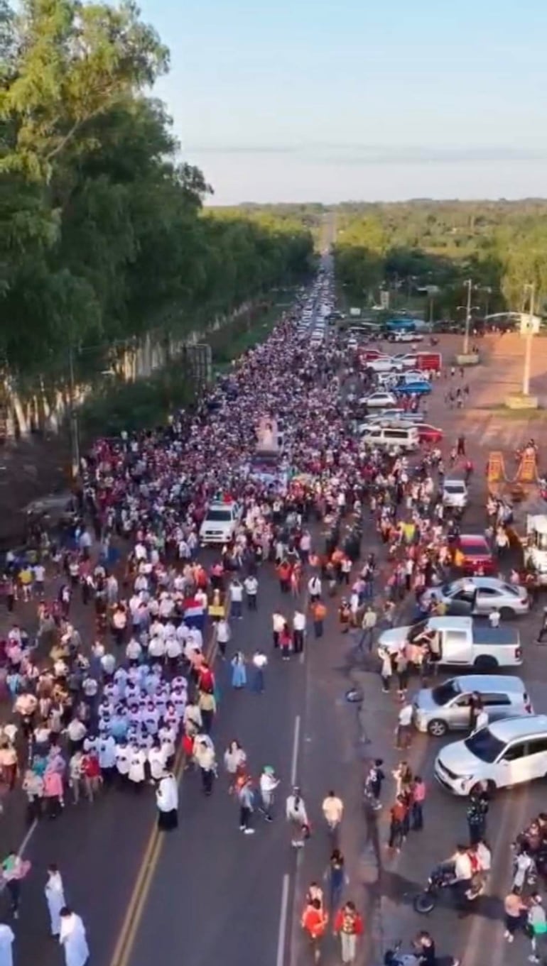 Multitud de personas vistiendo camisetas de colores en la caminata hacia la Virgen del Rosario, con banderas y árboles al fondo.