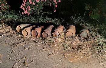 Cilindros metálicos oxidados alineados en la orilla de una carretera con vegetación de fondo.