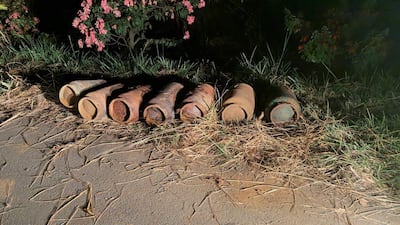 Cilindros metálicos oxidados alineados en la orilla de una carretera con vegetación de fondo.
