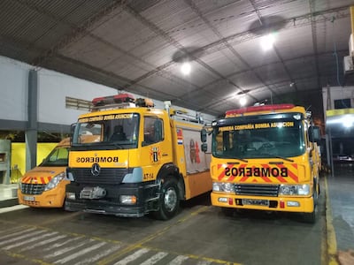 Dos camiones de bomberos de color amarillo y rojo estacionados en un garaje, pertenecientes a la Primera Compañía de Bomberos Asunción.