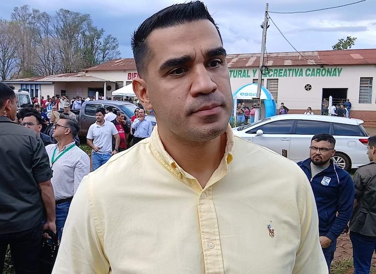 Luis Fernando Bernal en camisa amarilla, rodeado de personas en evento al aire libre, expresiones tranquilas y preocupadas en el público.