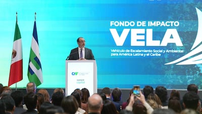 Hombre en traje oscuro y gafas habla tras un podio, con banderas de México y un gran panel detrás con el evento.