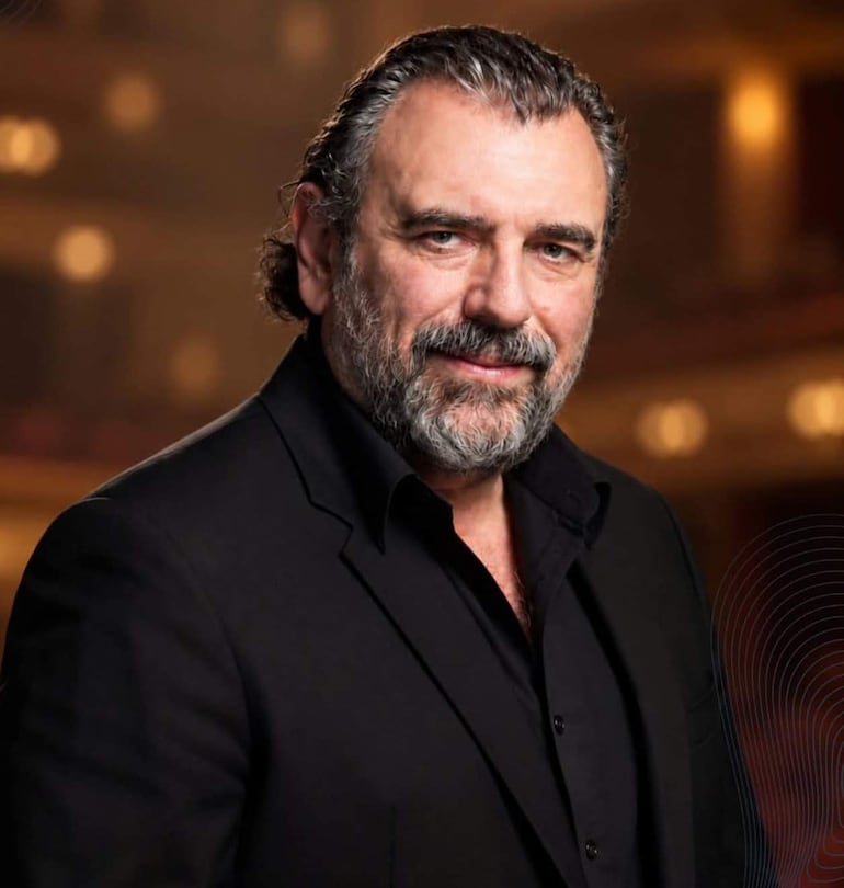 Luis Gorelik, con barba y saco negro, observa a la cámara en un ambiente suave y cálido de un teatro.