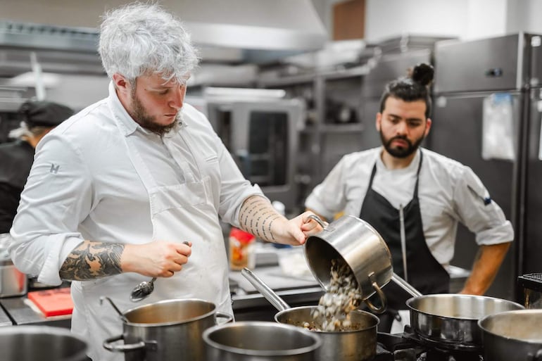 Alejandro Calcaterra en camisa blanca y delantal, mientras un segundo chef con barba observa, ambos en una cocina profesional.