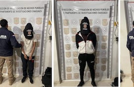 Dos agentes de policía junto a un detenido en la comisaría, el hombre esposado lleva camiseta blanca y pantalones oscuros.