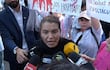 Rosanna González con camiseta negra, gesticulando intensamente rodeada de micrófonos, mientras personas sostienen carteles en protesta.