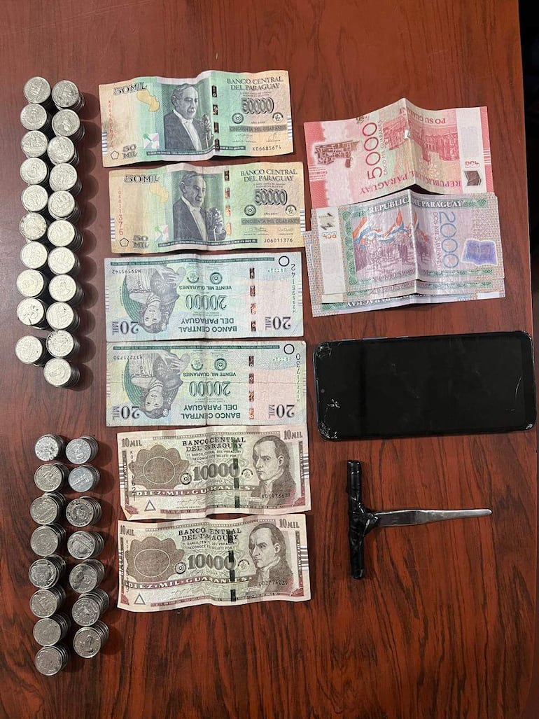 En una mesa, billetes y monedas paraguayas ordenadas; un smartphone negro en la esquina derecha.