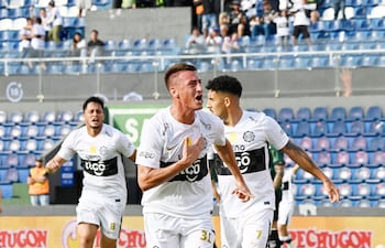 Jugadores de Olimpia celebran eufóricamente un gol, en un estadio lleno de espectadores entusiastas.