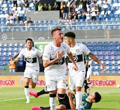 Jugadores de Olimpia celebran eufóricamente un gol, en un estadio lleno de espectadores entusiastas.
