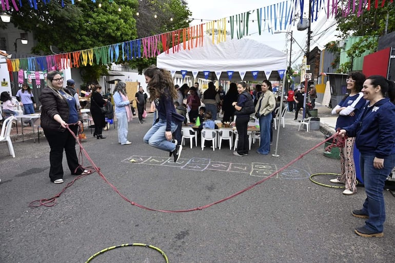 Grupo de personas sonriendo en evento al aire libre, con una joven saltando la cuerda y decoración colorida alrededor.