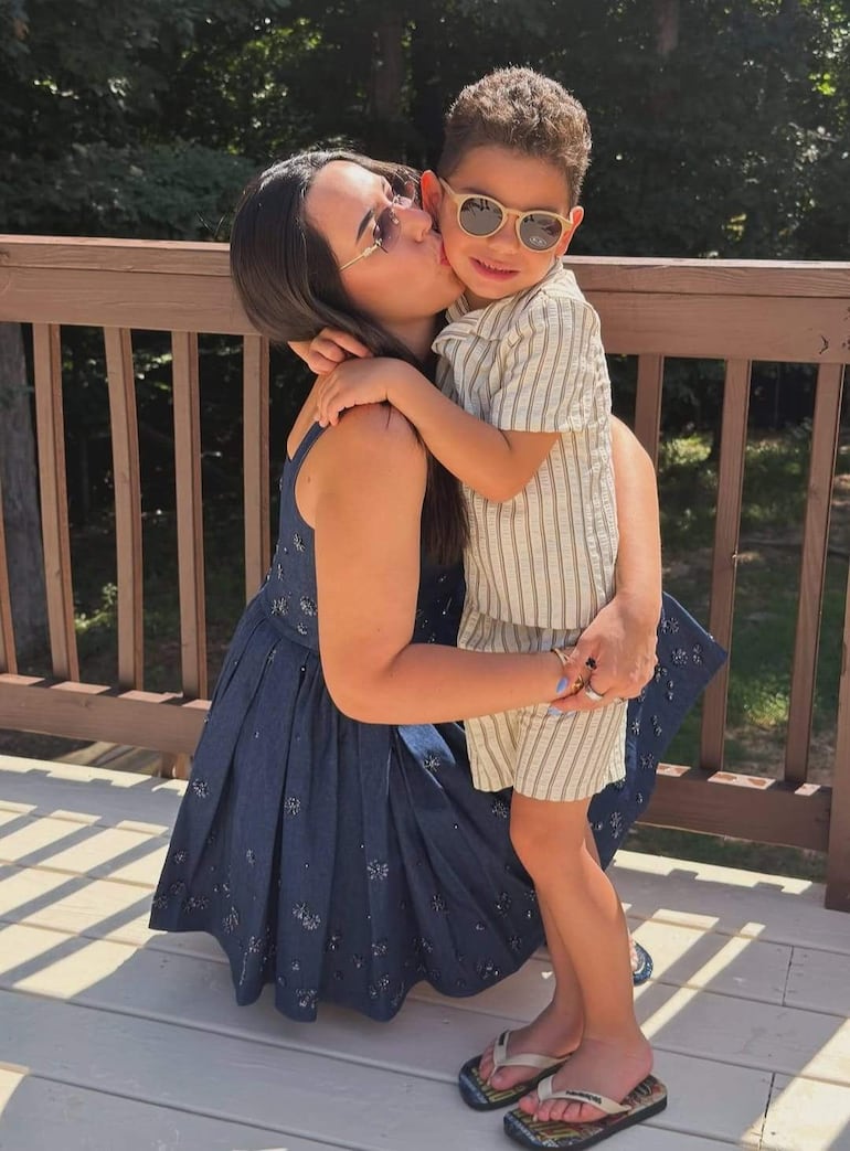 Mujer con vestido azul besa a un niño sonriente en un ambiente natural y soleado.