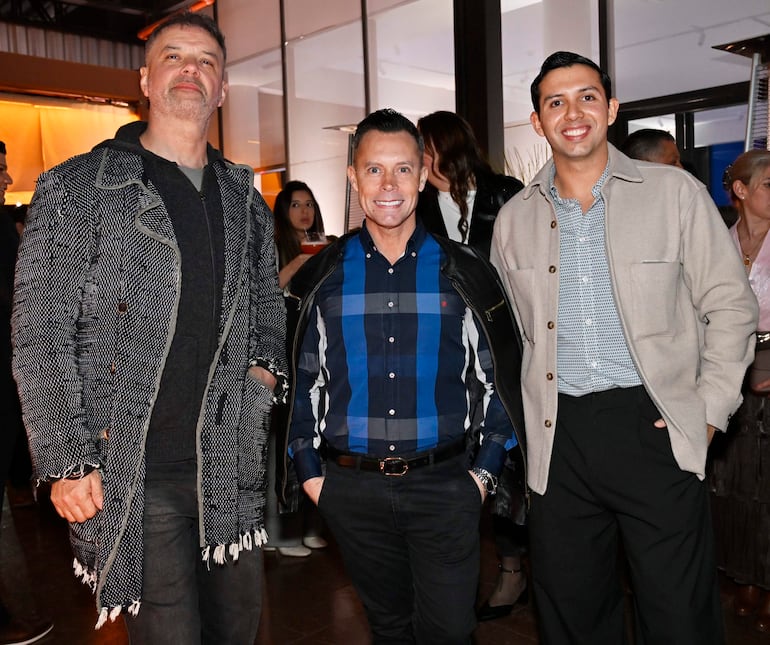 Tres hombres sonrientes en showroom, uno con chaqueta gruesa, otro en camisa a cuadros y el tercero en camisa clara, posando juntos.