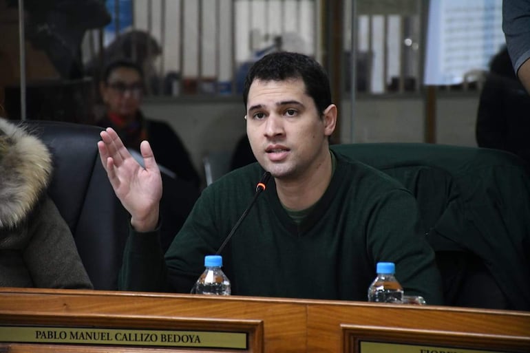 Pablo Callizo, con suéter verde oscuro, habla gesticulando en mesa con botellas de agua, mientras una mujer a su izquierda asiente.