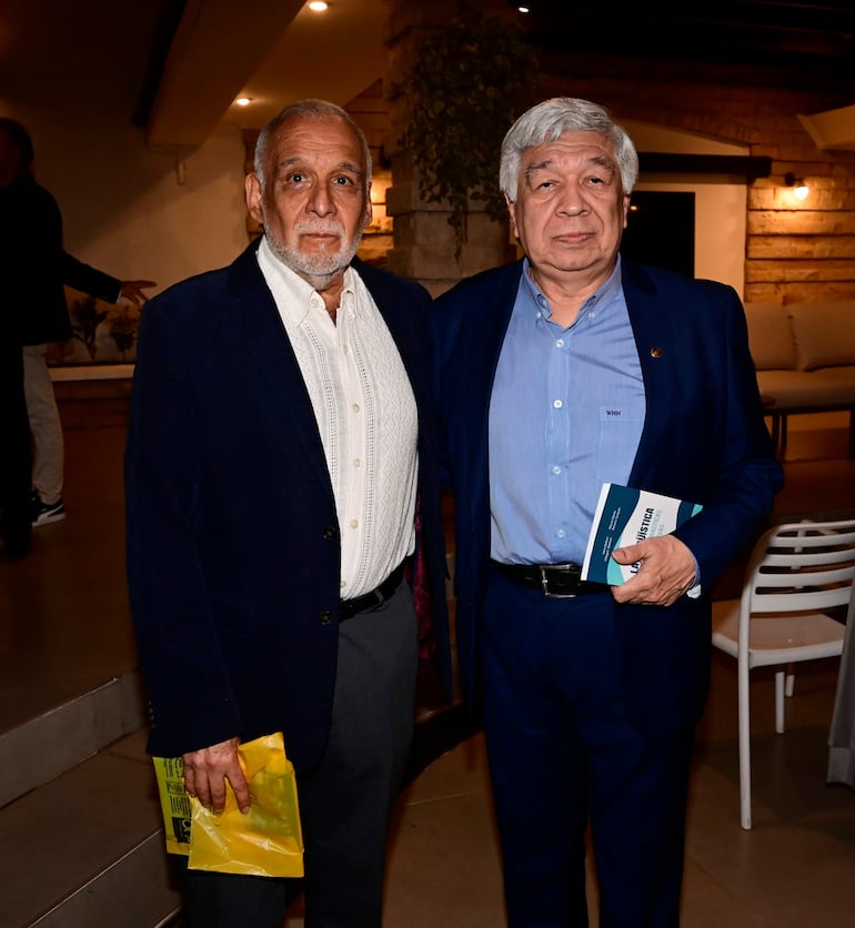 Ticio Escobar de saco oscuro y camisa blanca con bolsa amarilla, junto a Bernardo Neri Farina de saco azul y libro en mano.