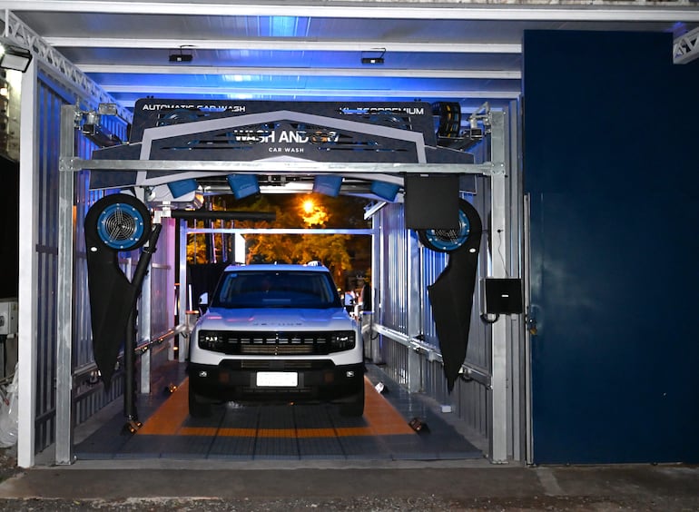 Vehículo grande a punto de ingresar al túnel de lavado en instalaciones de Wash and Go Car Wash iluminadas por la noche.