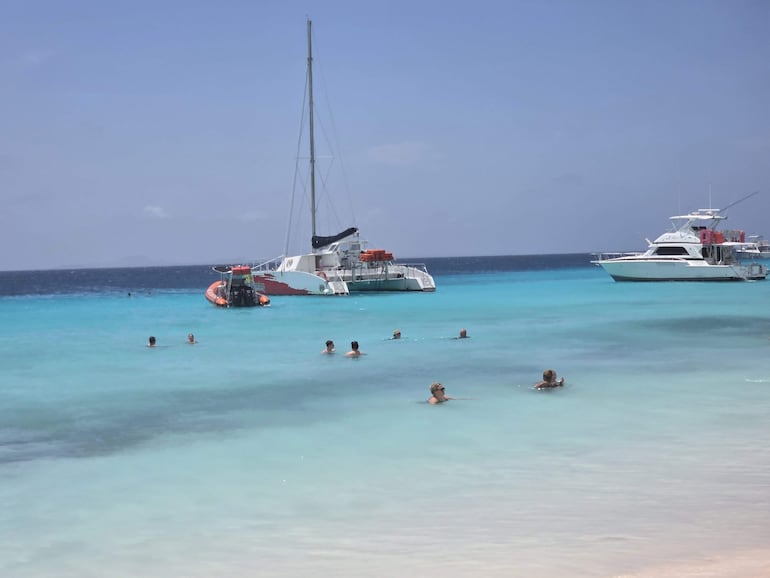 Nadadores en aguas cristalinas, disfrutando del sol en un ambiente costero y alegre, con yates anclados al fondo.