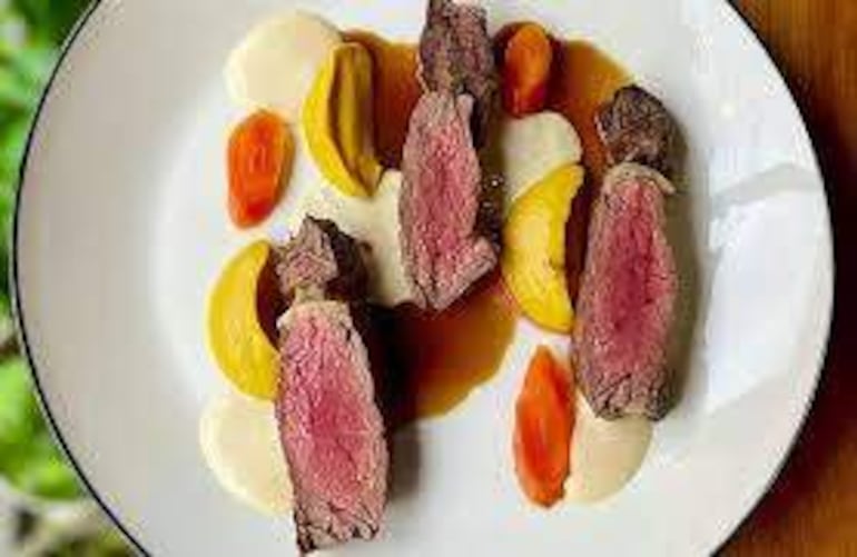 Plato gourmet con trozos de carne asada, salsas de colores, en un ambiente elegante y bien iluminado.