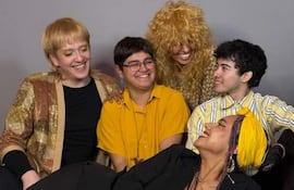 Cinco personas sonrientes en fondo gris: mujer con pañuelo amarillo y chico alegre, con atuendos amarillos y oscuros.