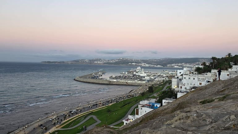 Extensa vista del mar y la zona urbana de Tánger, con edificios y colinas al fondo, iluminada por un atardecer suave.
