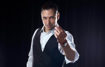 Hombre de pie con camisa blanca y chaleco negro, mostrando confianza en un fondo oscuro.