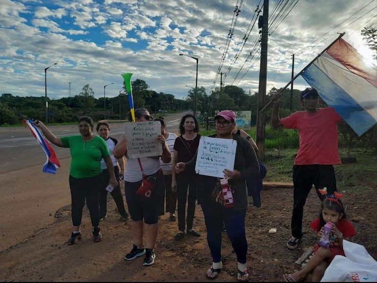 Ocho manifestantes, incluyendo a mujeres con pancartas y banderas paraguayas, protestan en un entorno natural.