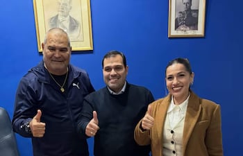 Chilavert en chaqueta negra, Achucarro Gill en vestimenta formal y Maldonado con chaqueta marrón, todos sonriendo en entorno azul.