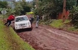 Cuatro hombres en un camino de barro, uno empujando un vehículo atascado, rodeados de vegetación en área rural.