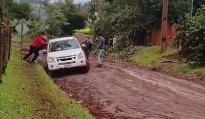 Cuatro hombres en un camino de barro, uno empujando un vehículo atascado, rodeados de vegetación en área rural.